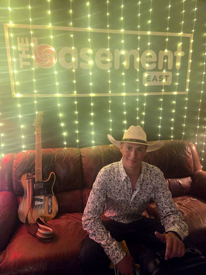 Davis seated on a leather couch under The Basement East sign with a telecaster beside him