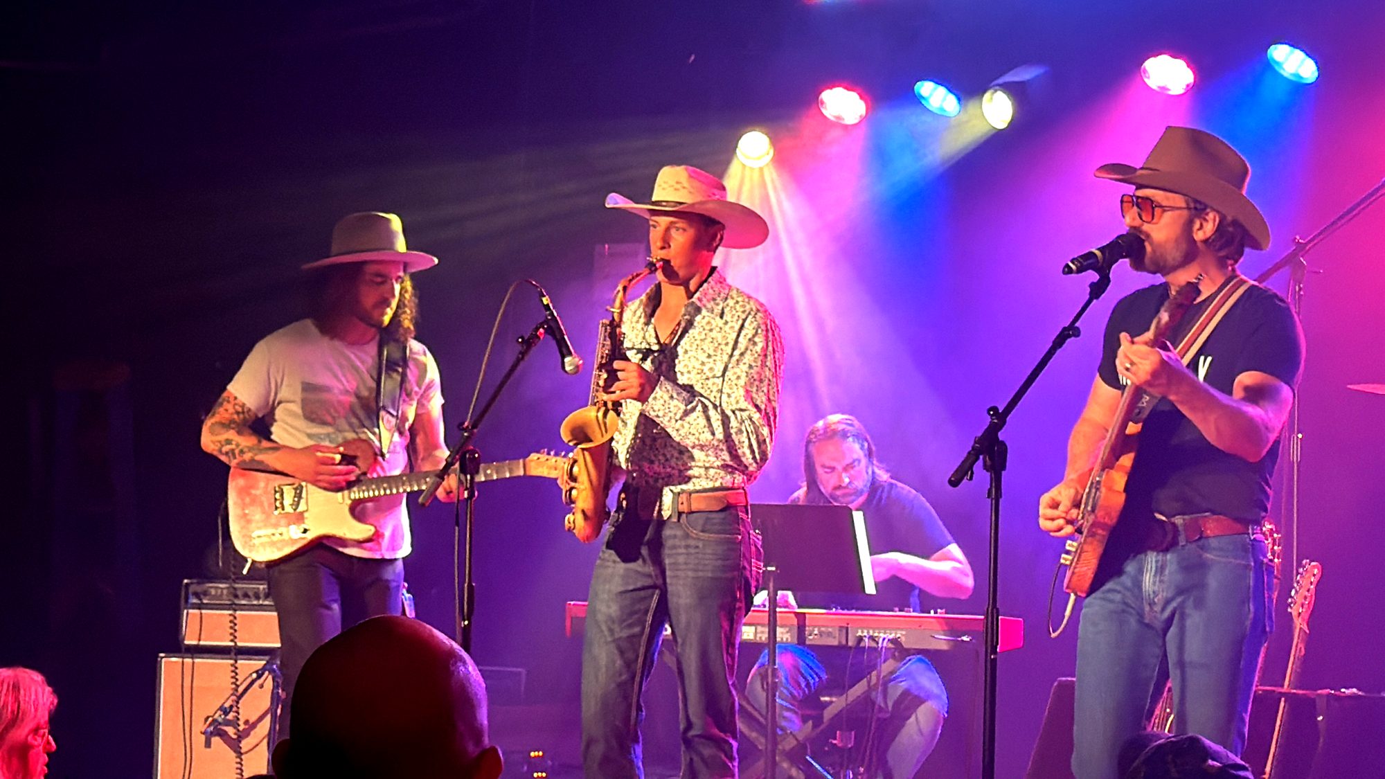 Davis Kidder playing alto saxophone on stage under magenta and blue lights with a full band